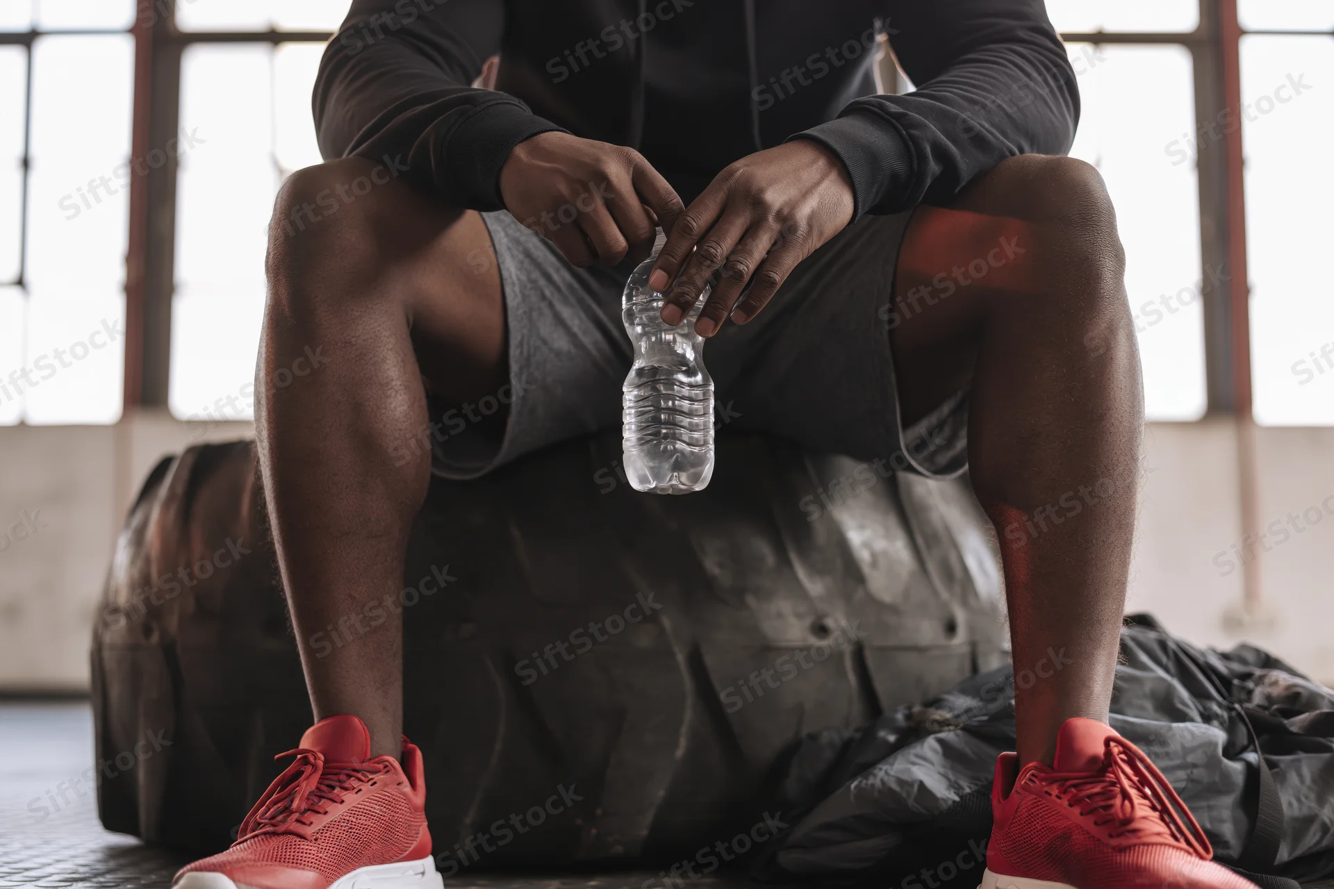 Young african american man sitting on large training tire holding water bottle in gym