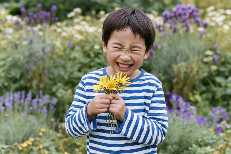 Young asian boy laughing while holding a small bouquet of yellow daisies in a garden