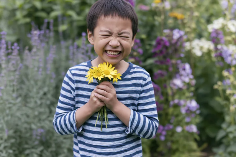 Young asian boy laughing while holding a small bouquet of yellow daisies in a garden