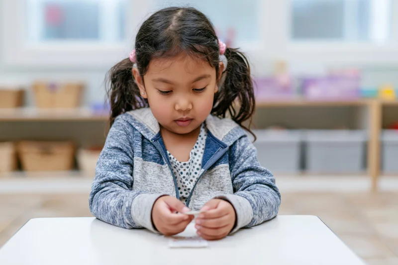 Young asian girl concentrating on a small card at a white table in a classroom
