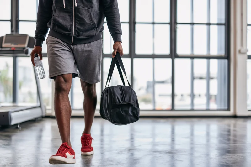 Young black man walking through gym carrying duffel bag and water bottle