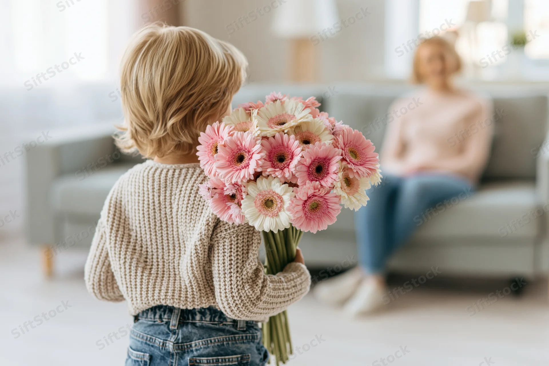 Young blond child holding bouquet of pink and white gerber flowers facing mother on sofa in living room