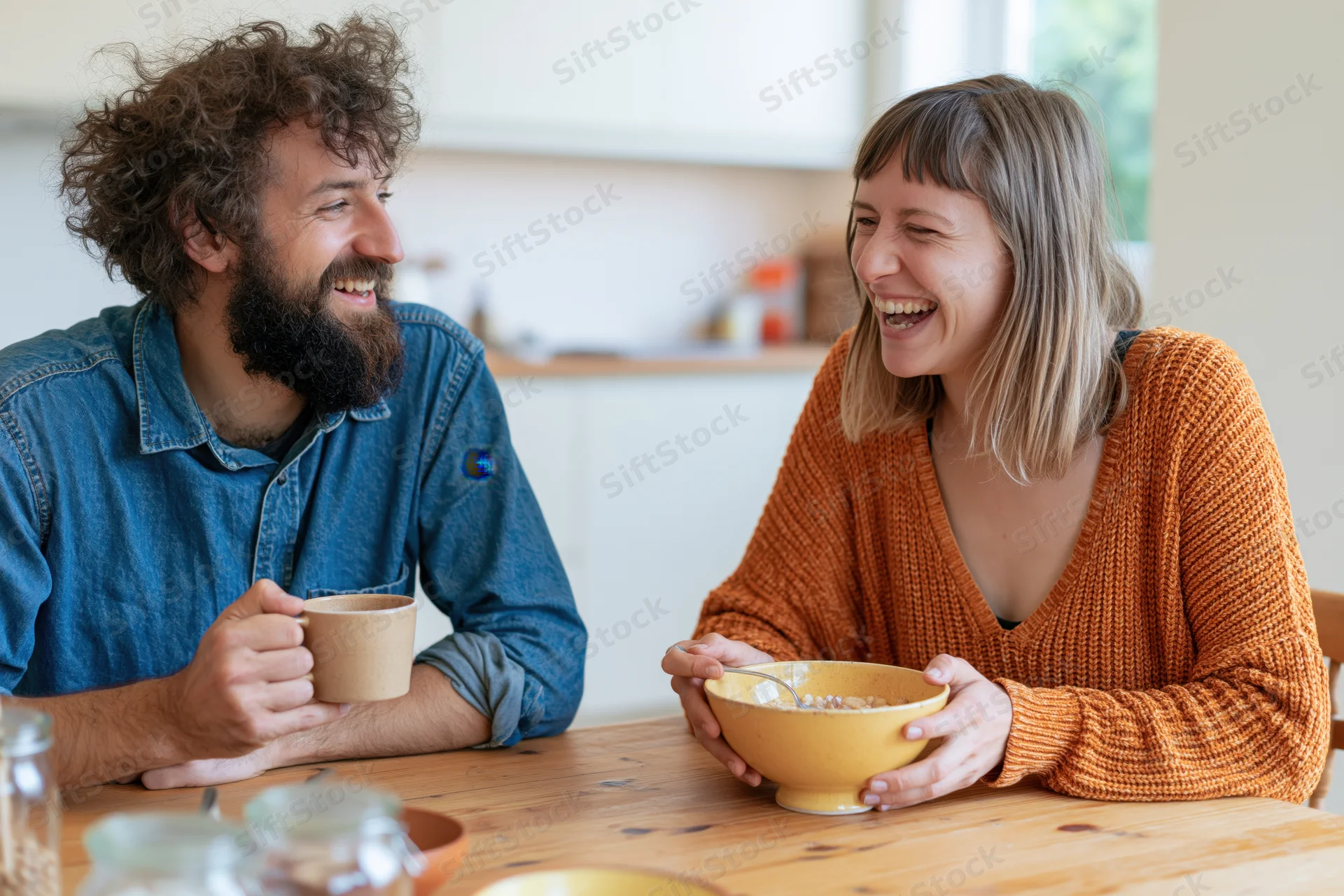 Young couple laughing and sharing breakfast at a wooden kitchen table
