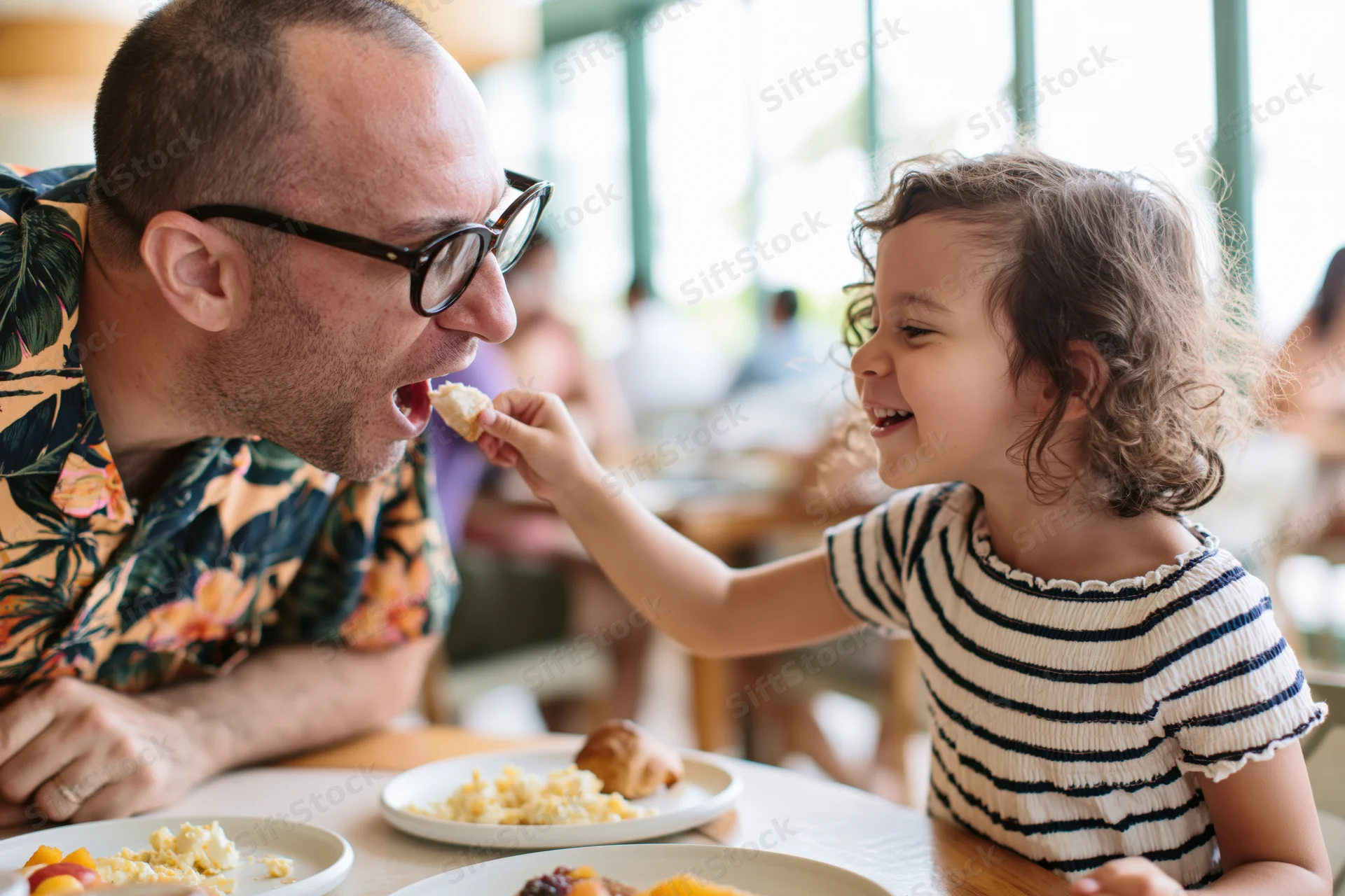 Young daughter feeding her father a piece of bread at a restaurant table