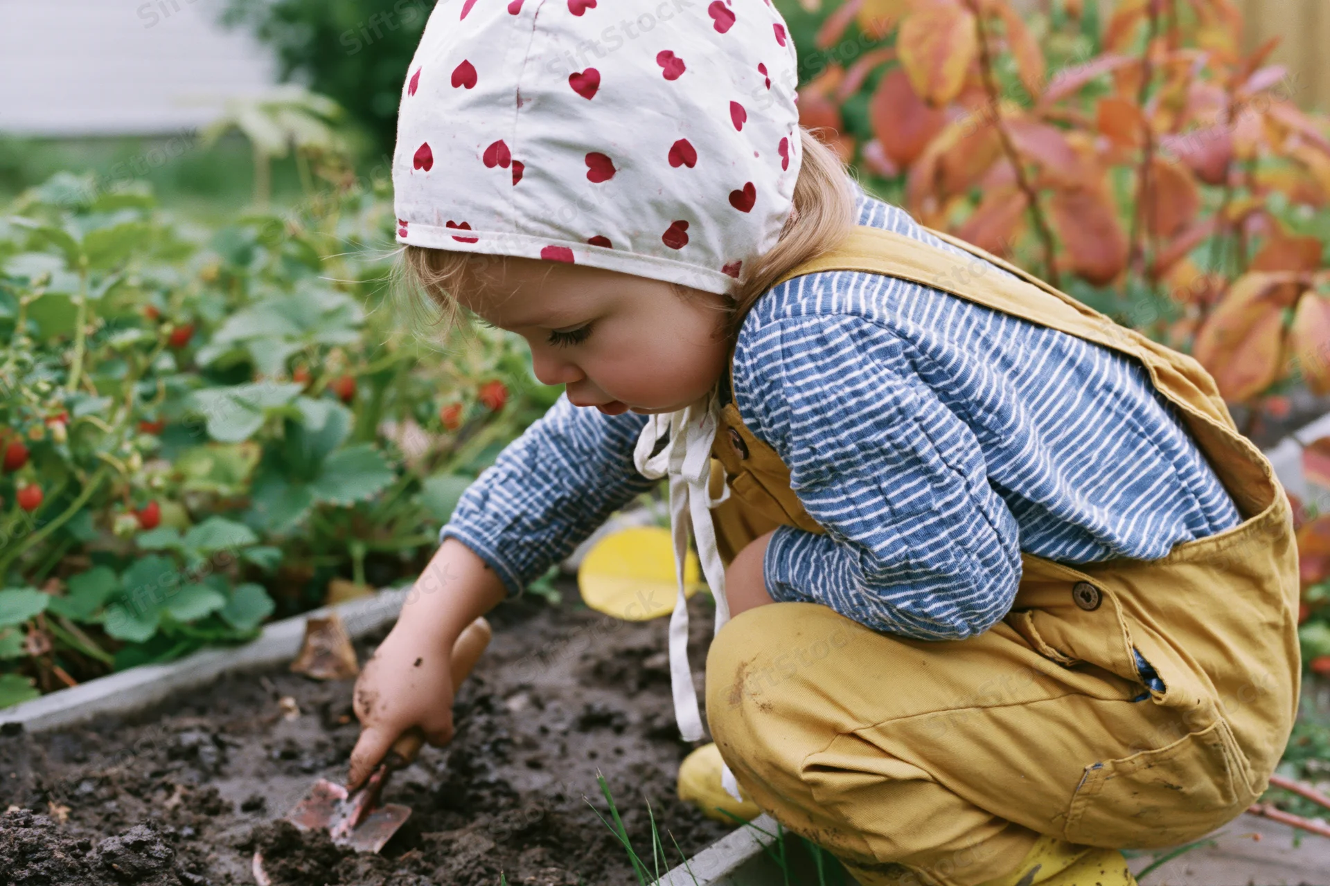 Young girl crouching beside a raised garden bed digging soil with a trowel