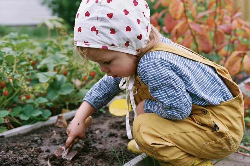 Young girl crouching beside a raised garden bed digging soil with a trowel