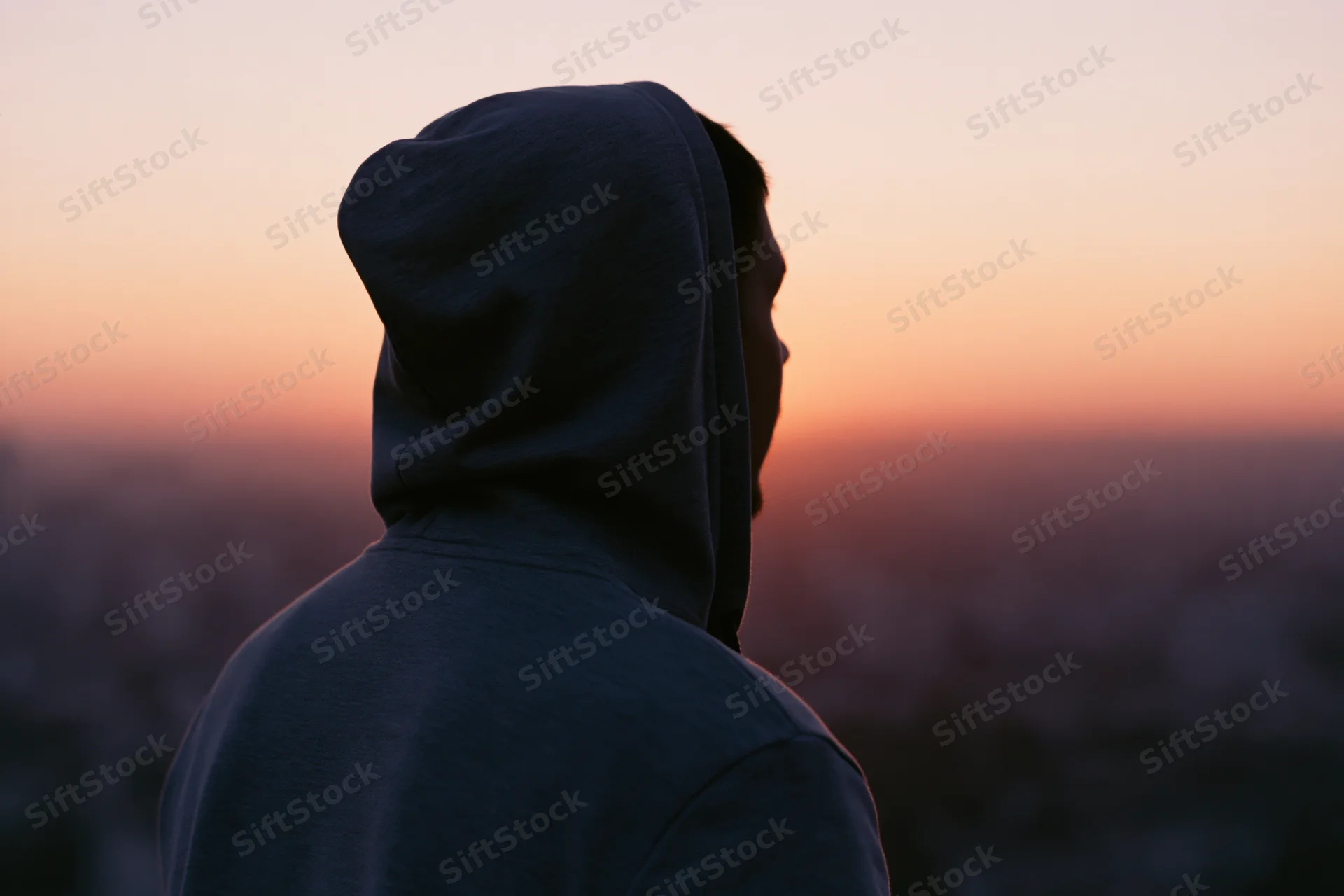 Man in hooded sweatshirt seen from behind overlooking cityscape at sunset
