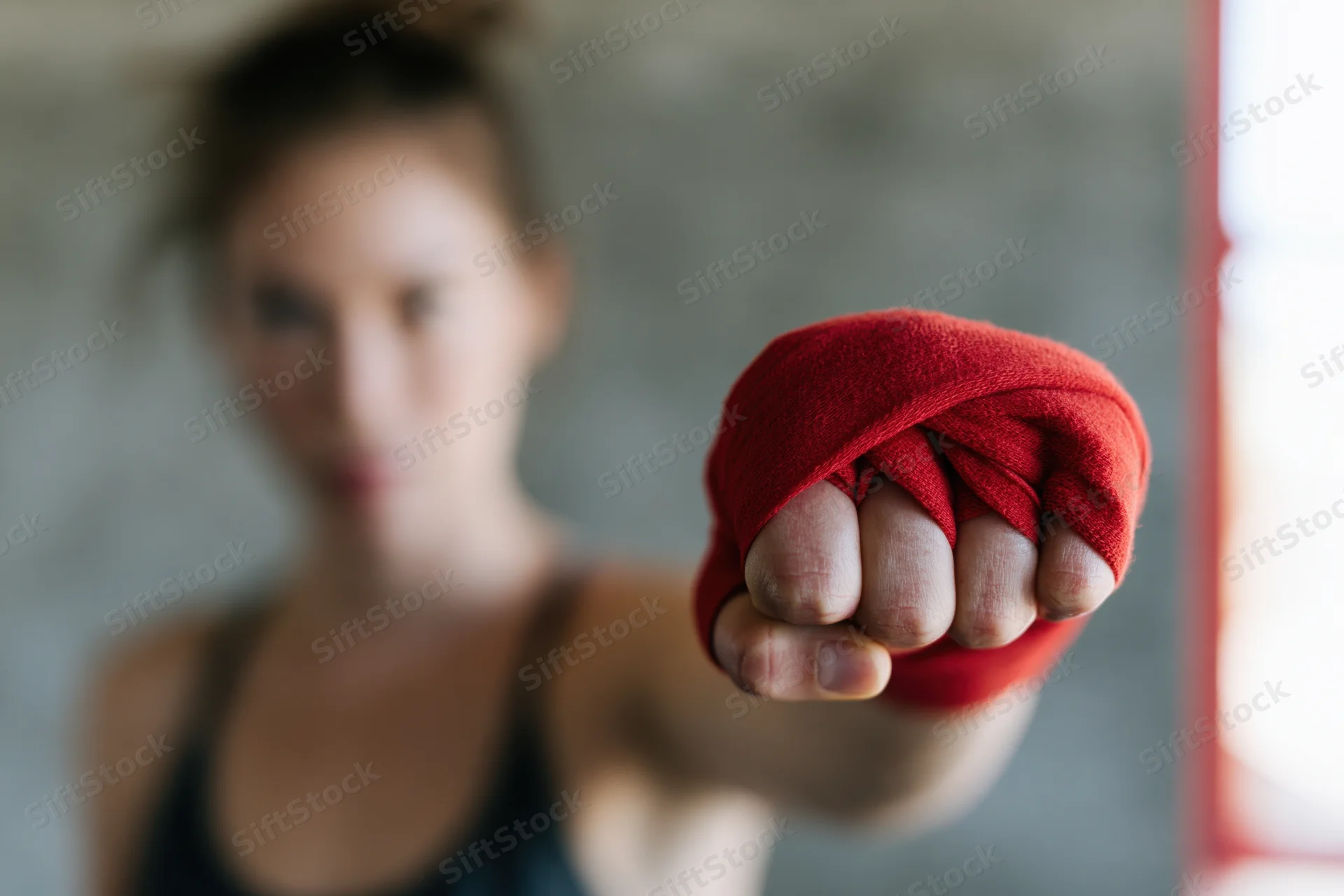 Woman boxer throwing a straight punch toward the camera with red hand wrap in focus
