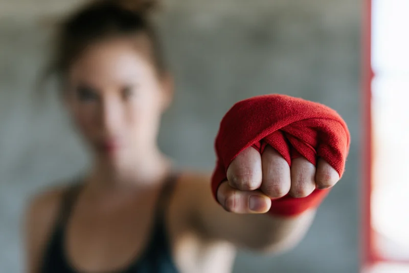 Woman boxer throwing a straight punch toward the camera with red hand wrap in focus