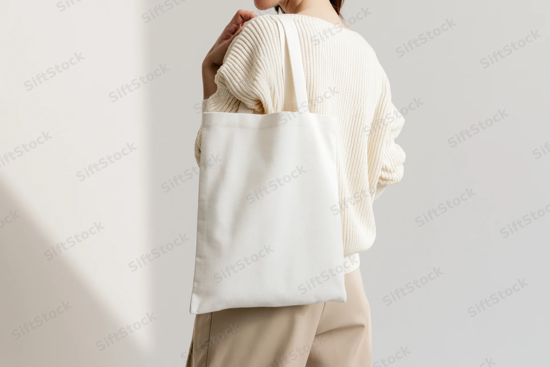 Woman carrying a plain white canvas tote bag over her shoulder in a minimalist studio setting