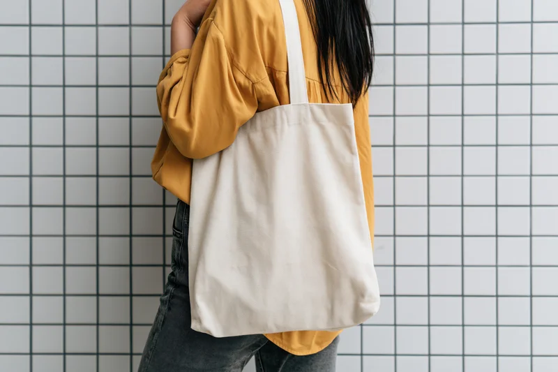 Young woman carrying a plain natural cotton tote bag over her shoulder against a tiled wall