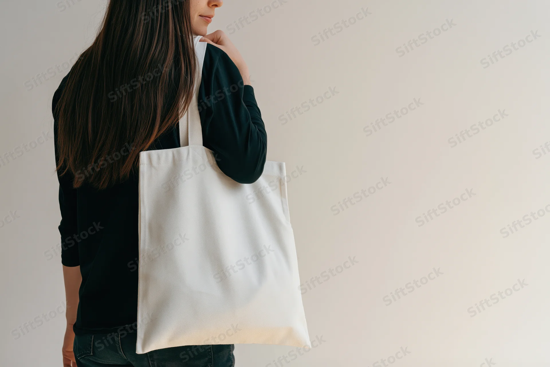 Woman carrying a plain white cotton tote bag over her shoulder in a studio setting