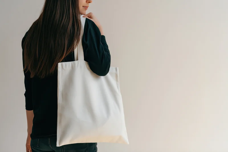 Woman carrying a plain white cotton tote bag over her shoulder in a studio setting