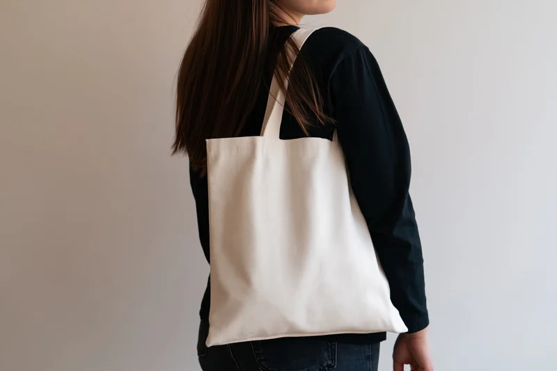 Woman carrying a plain white cotton tote bag over her shoulder in casual clothing