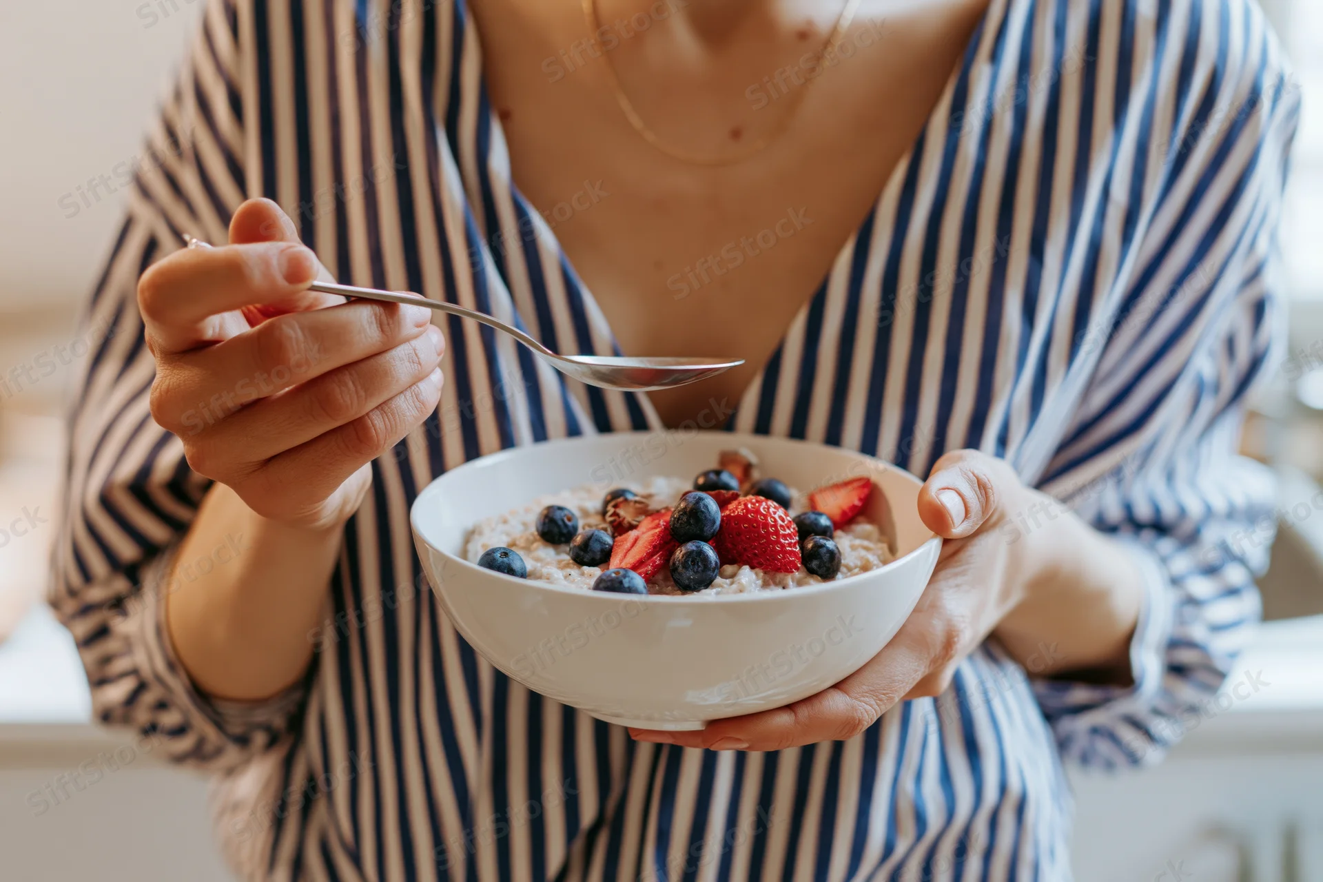 Woman holding a bowl of oatmeal topped with blueberries and strawberries in a kitchen