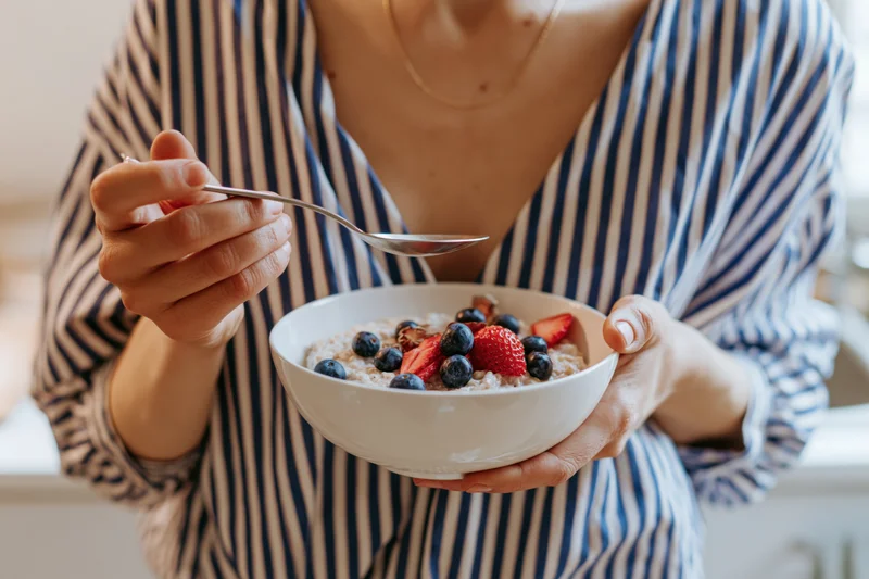 Woman holding a bowl of oatmeal topped with blueberries and strawberries in a kitchen