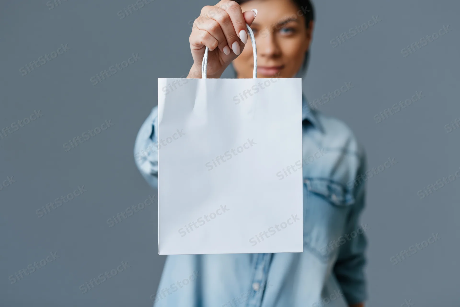 Woman holding white paper shopping bag in front of gray background