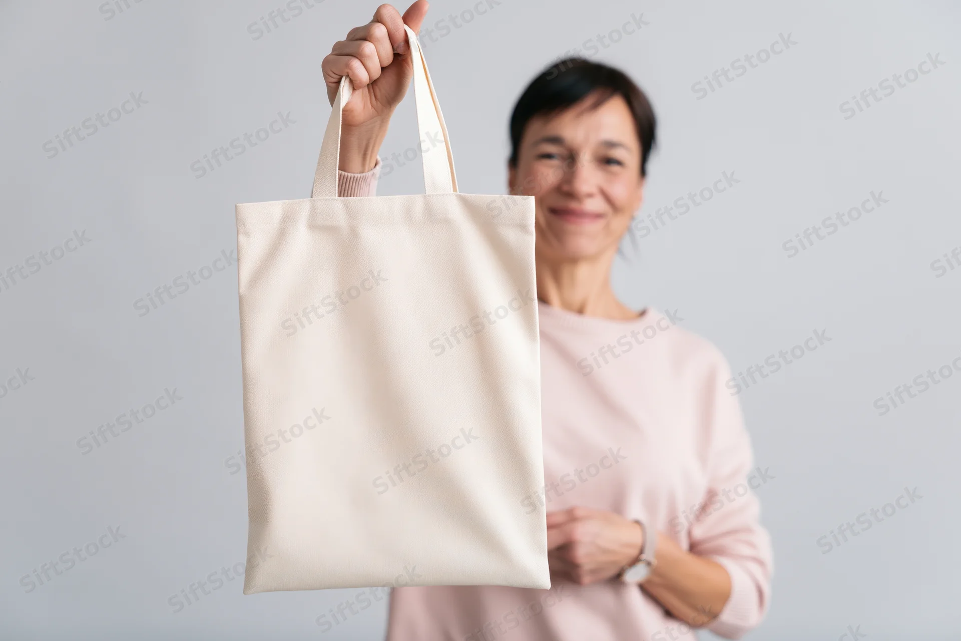 Woman holding a blank canvas tote bag in front of a light gray background