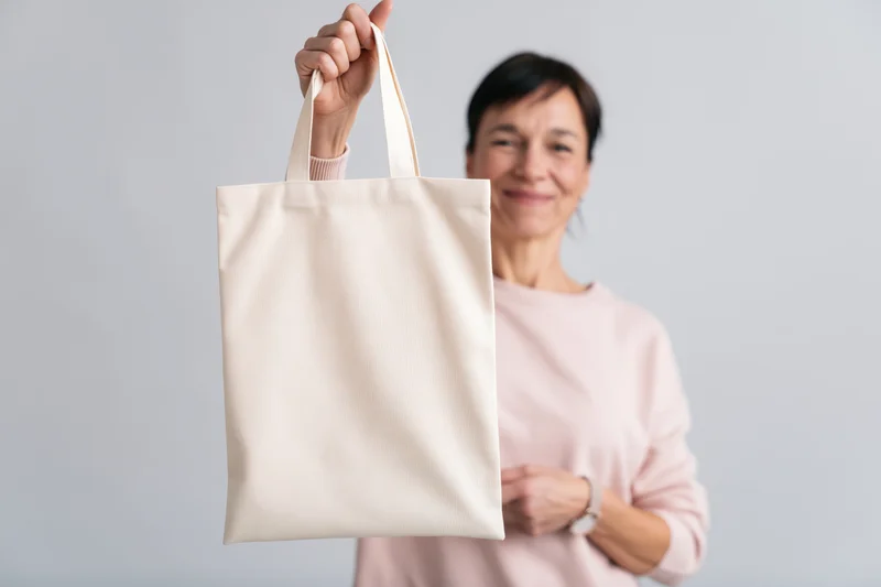 Woman holding a blank canvas tote bag in front of a light gray background