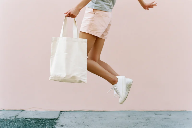 Woman mid-jump holding cream canvas tote bag outdoors