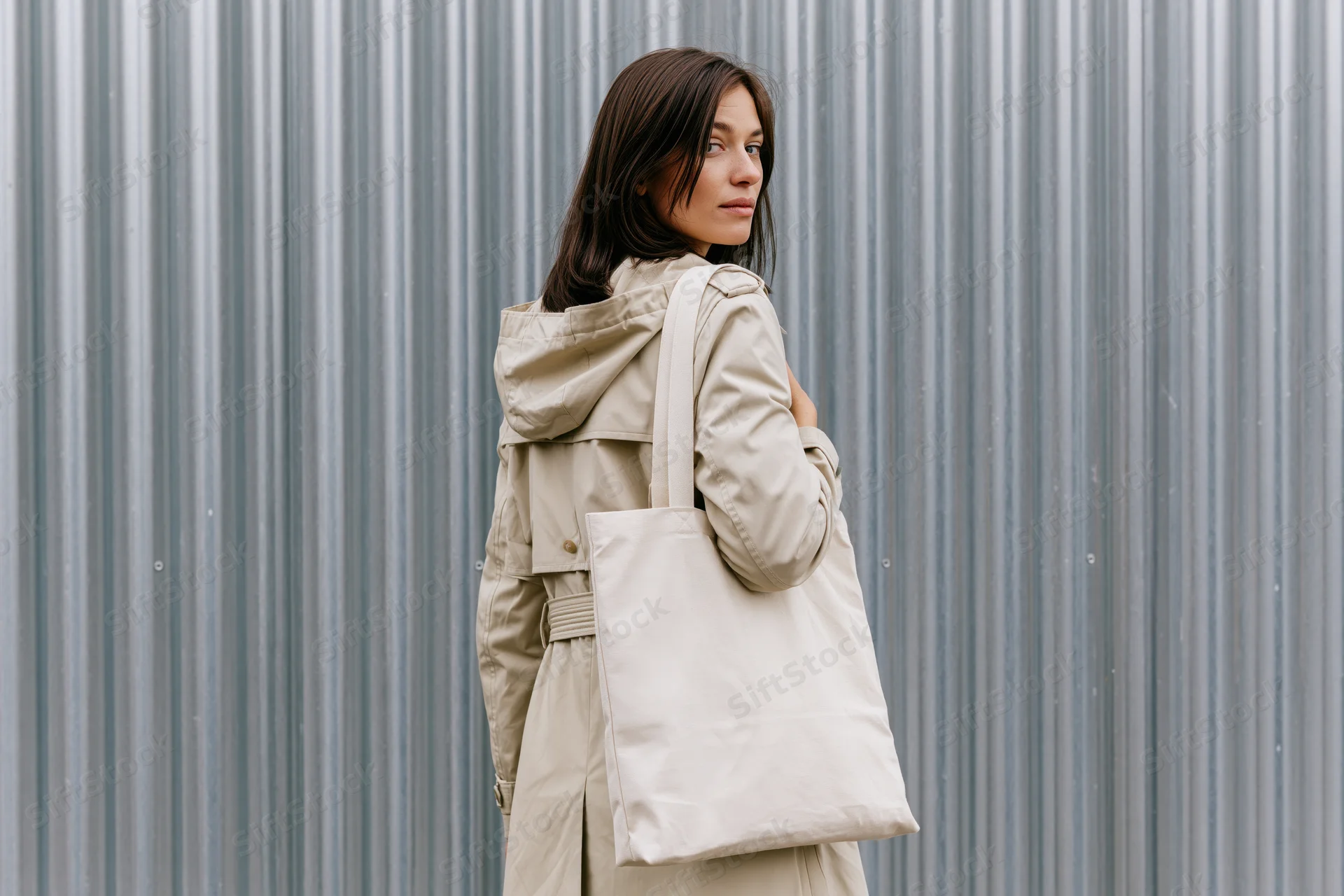 Young woman carrying a plain canvas tote bag over her shoulder, standing in front of a corrugated metal wall