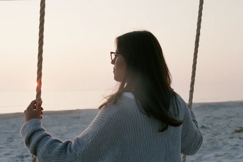 Woman sitting on rope swing at beach during sunset
