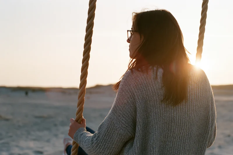 Young woman sitting on a rope swing at sunset on a sandy beach