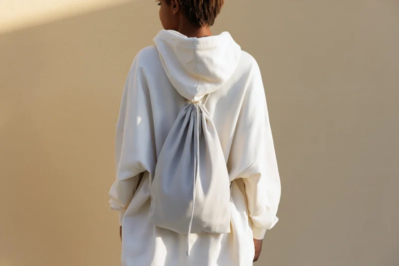 Woman from behind wearing white oversized hoodie with drawstring backpack against beige wall