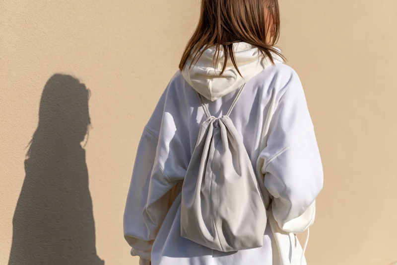 Young woman from behind wearing white oversized hoodie with backpack against beige wall
