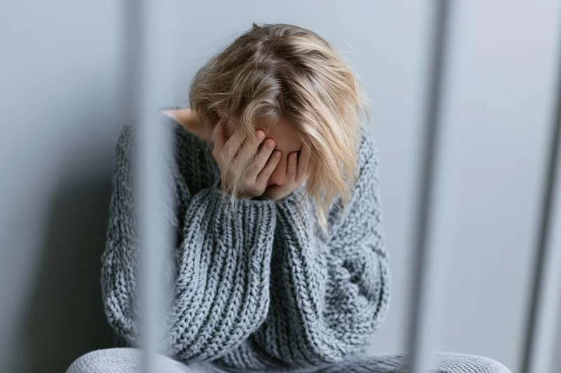 Young woman sitting on the floor against a grey wall with hands covering her face