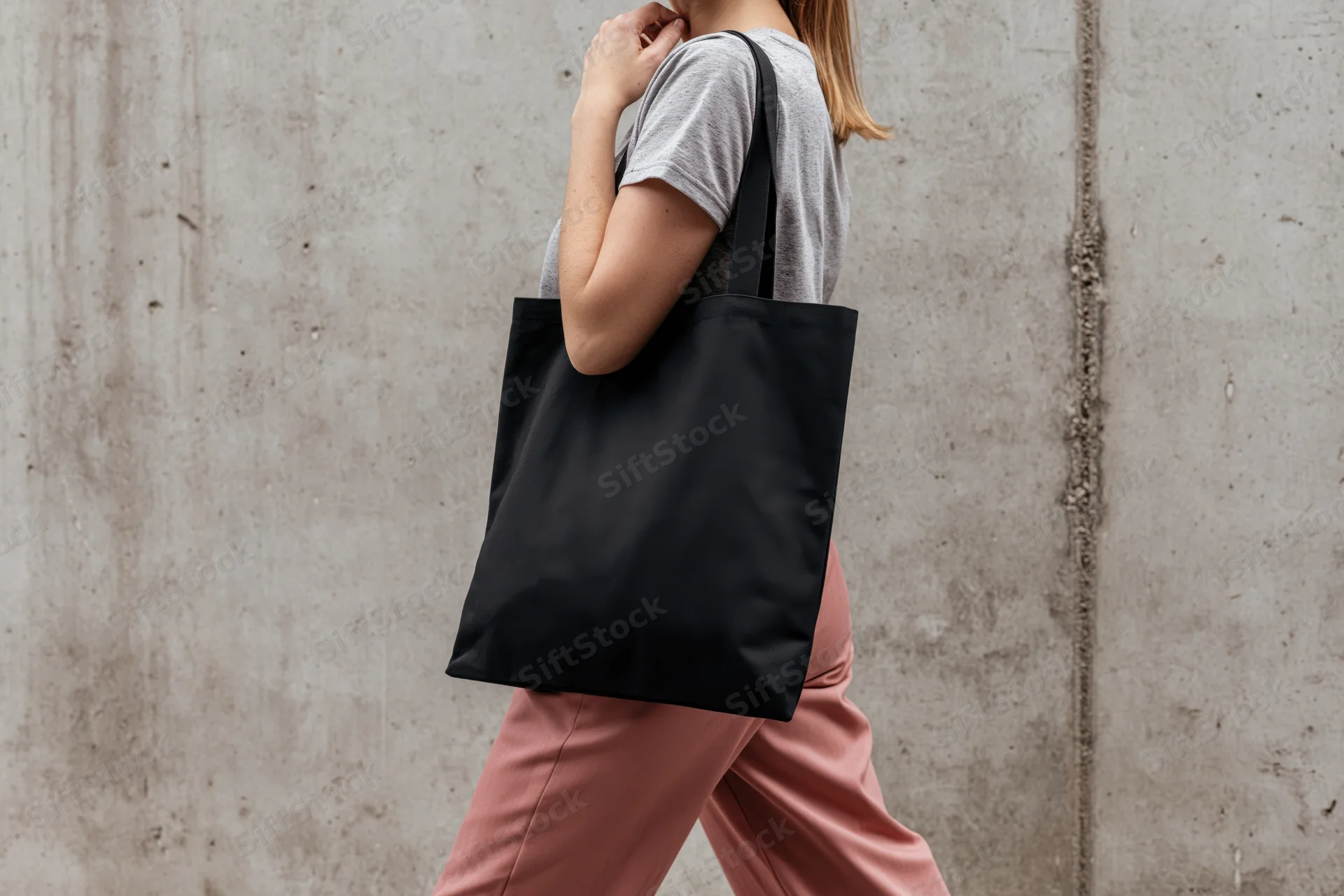 Woman walking with black tote bag over shoulder against concrete wall