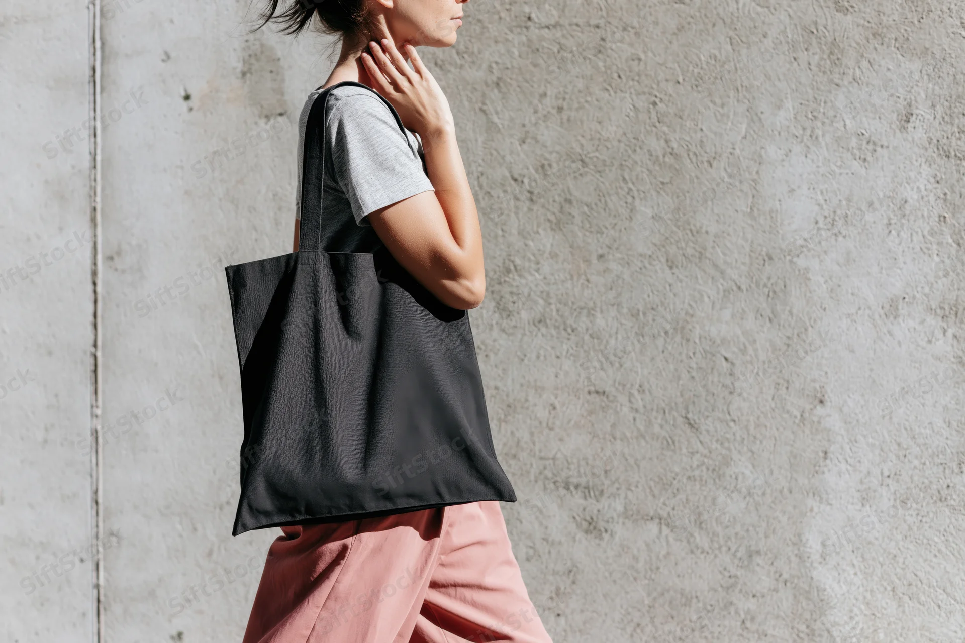 Woman walking with tote bag against concrete wall in urban setting