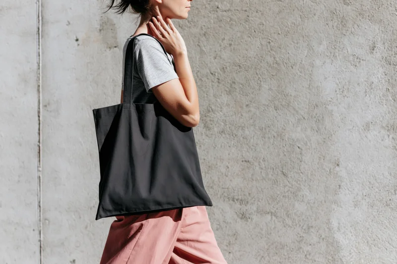 Woman walking with tote bag against concrete wall in urban setting