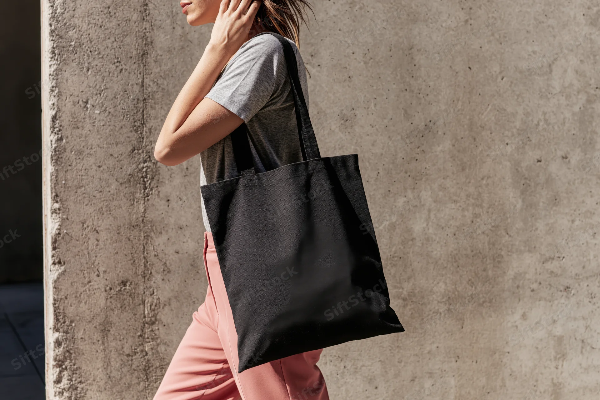 Woman walking outdoors with black tote bag over shoulder near concrete wall