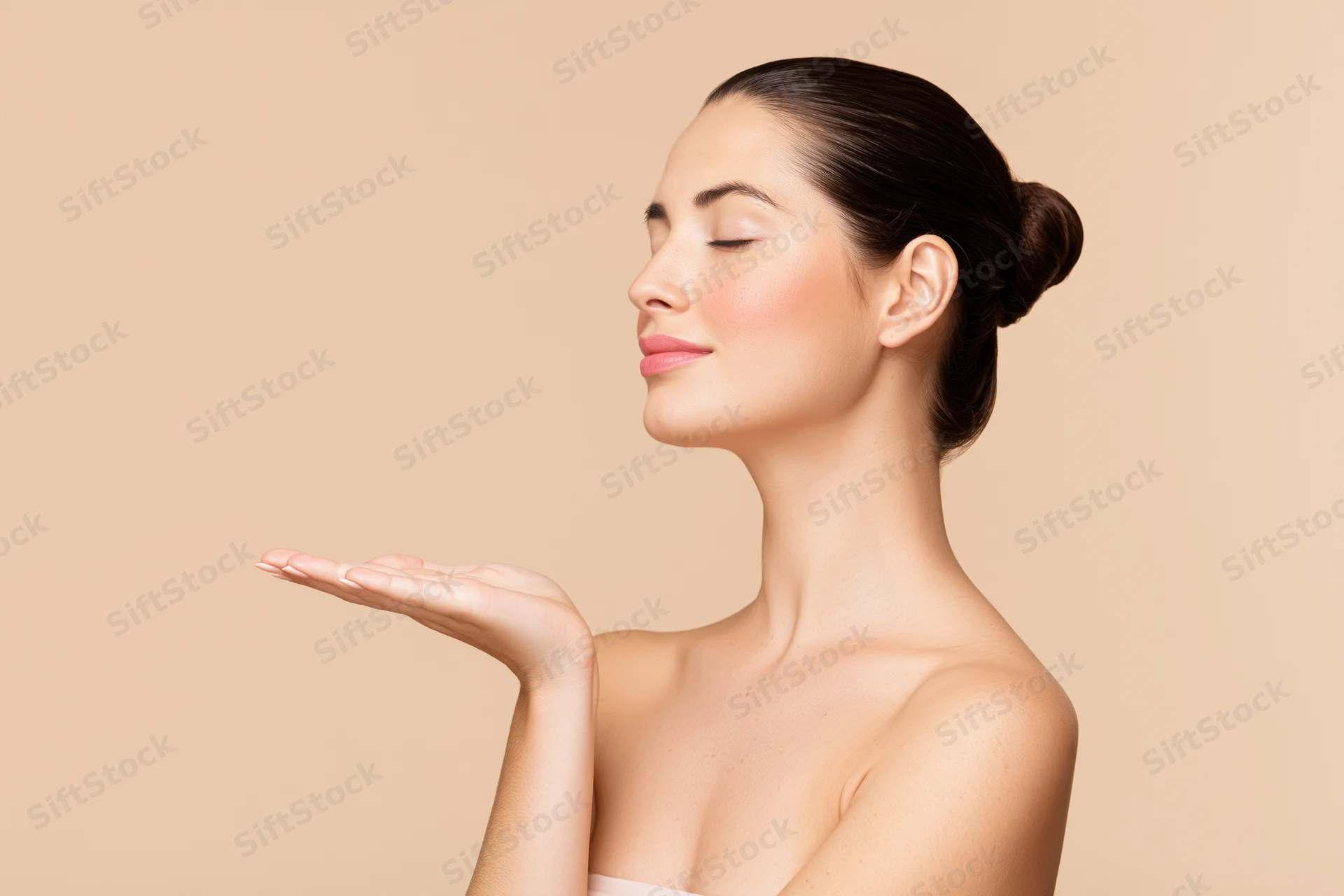Woman with dark hair in a sleek bun, eyes closed, holding hand out, side profile against beige background