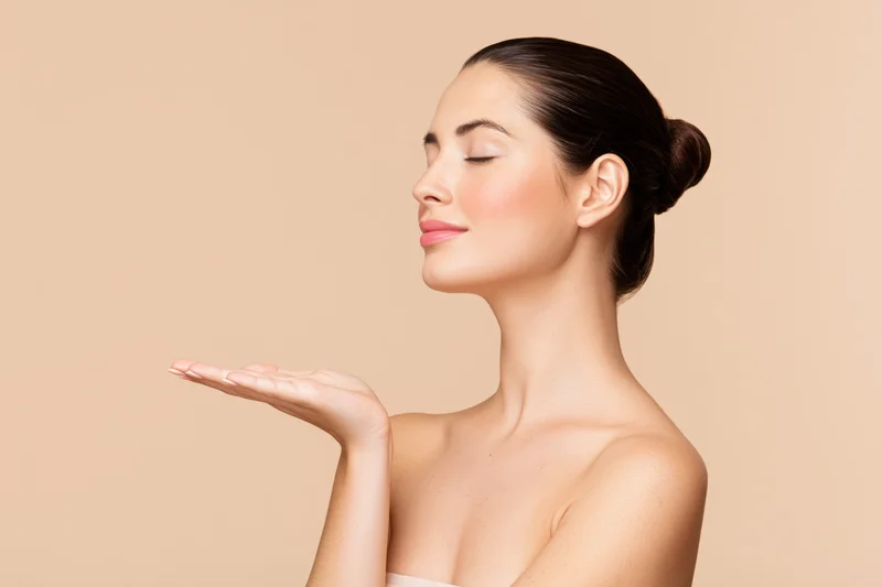 Woman with dark hair in a sleek bun, eyes closed, holding hand out, side profile against beige background