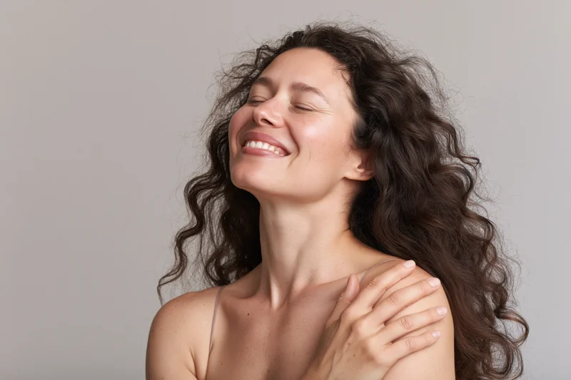 Woman smiling with eyes closed, hand on shoulder, in studio setting