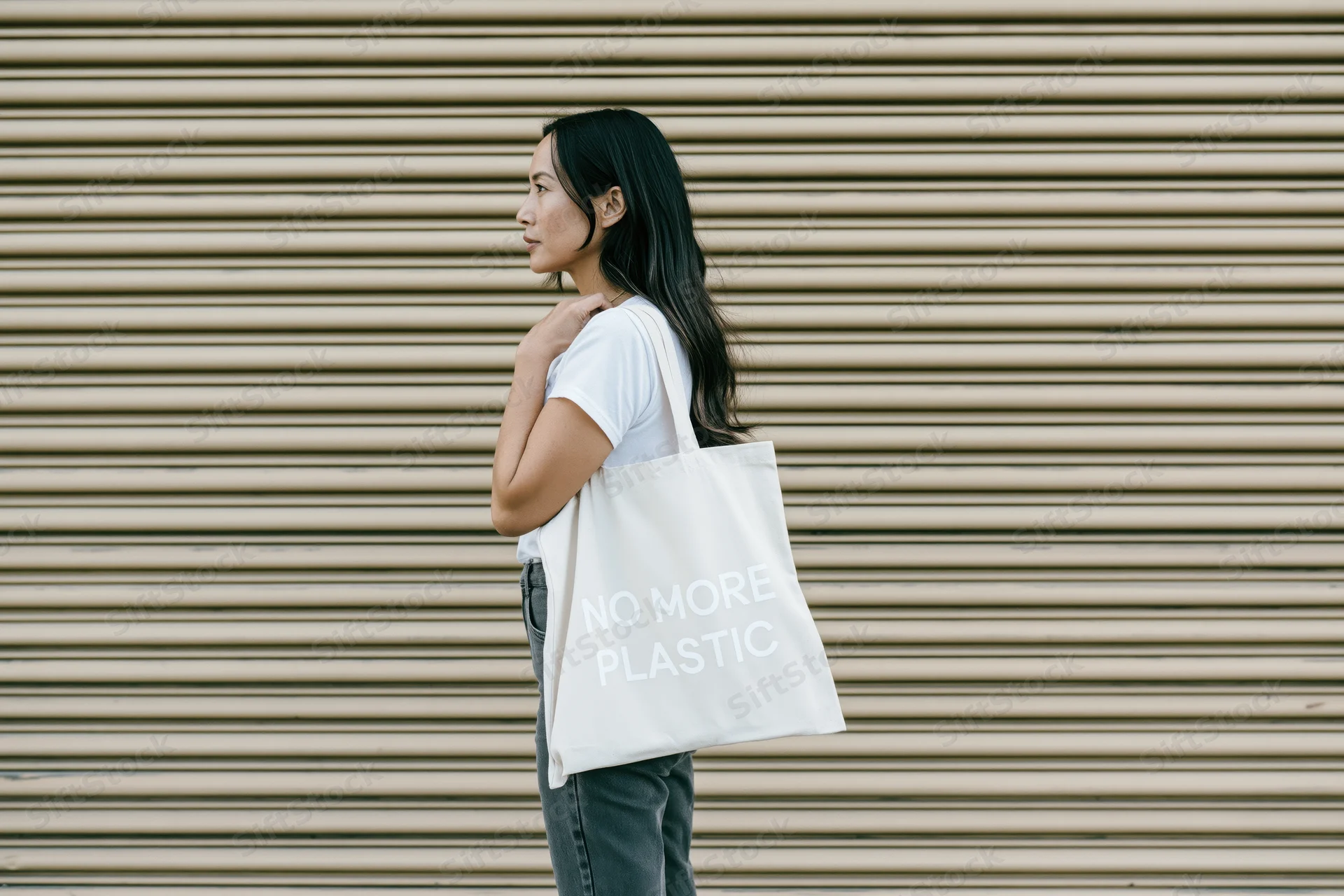 Woman in profile holding a tote bag with no more plastic text against a metal shutter