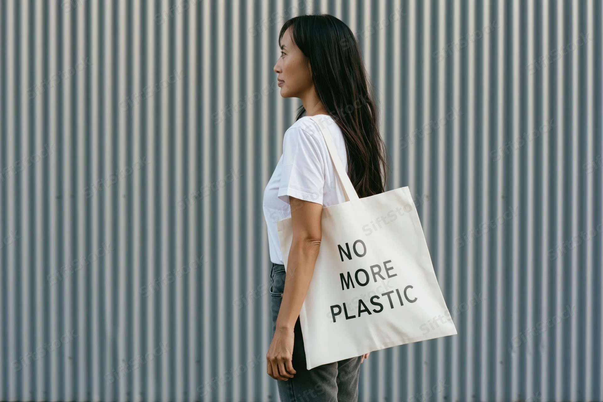 Young woman in profile carrying a tote bag with no more plastic message against corrugated metal wall