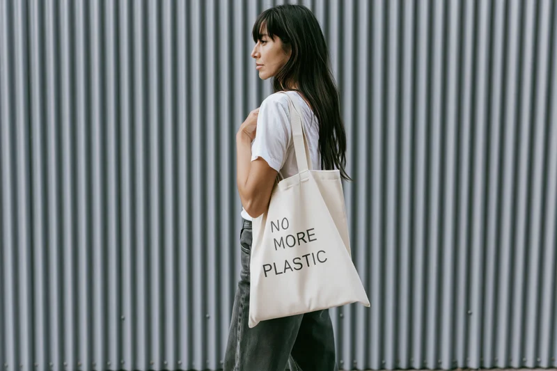 Woman in profile carrying a tote bag with no more plastic message against corrugated metal wall
