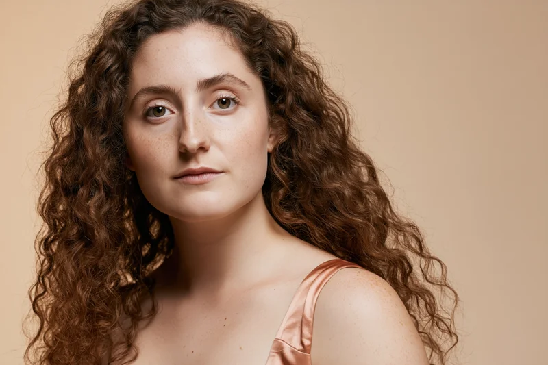 Young woman with long curly brown hair looking directly at camera in studio portrait
