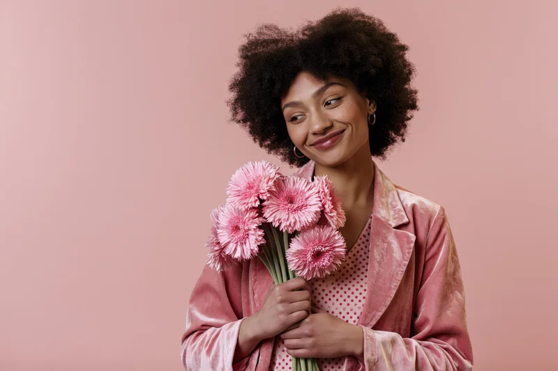 Young woman with afro holding pink flowers in studio setting