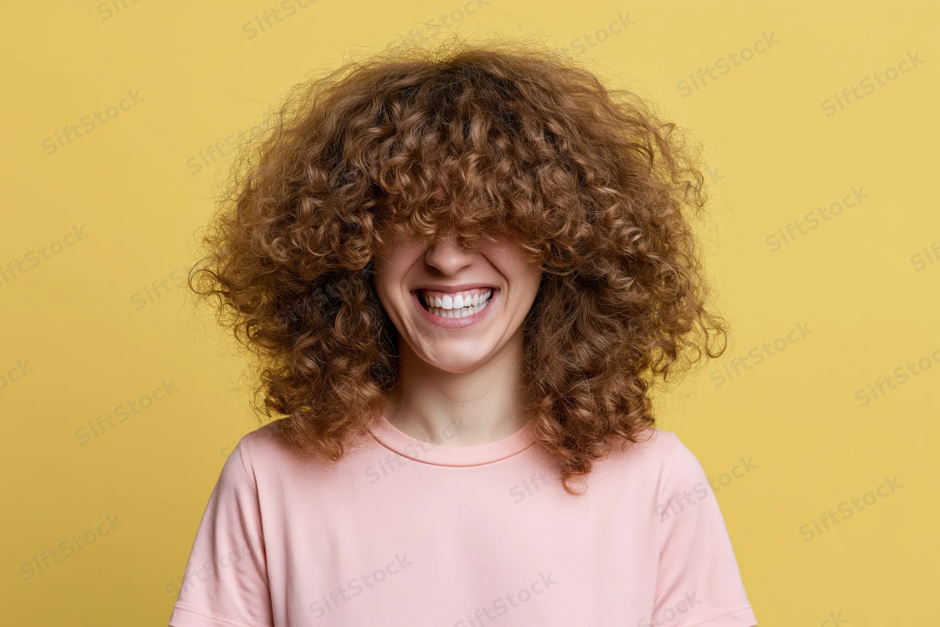 Young woman with voluminous curly brown hair smiling against yellow background