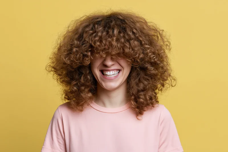 Young woman with voluminous curly brown hair smiling against yellow background