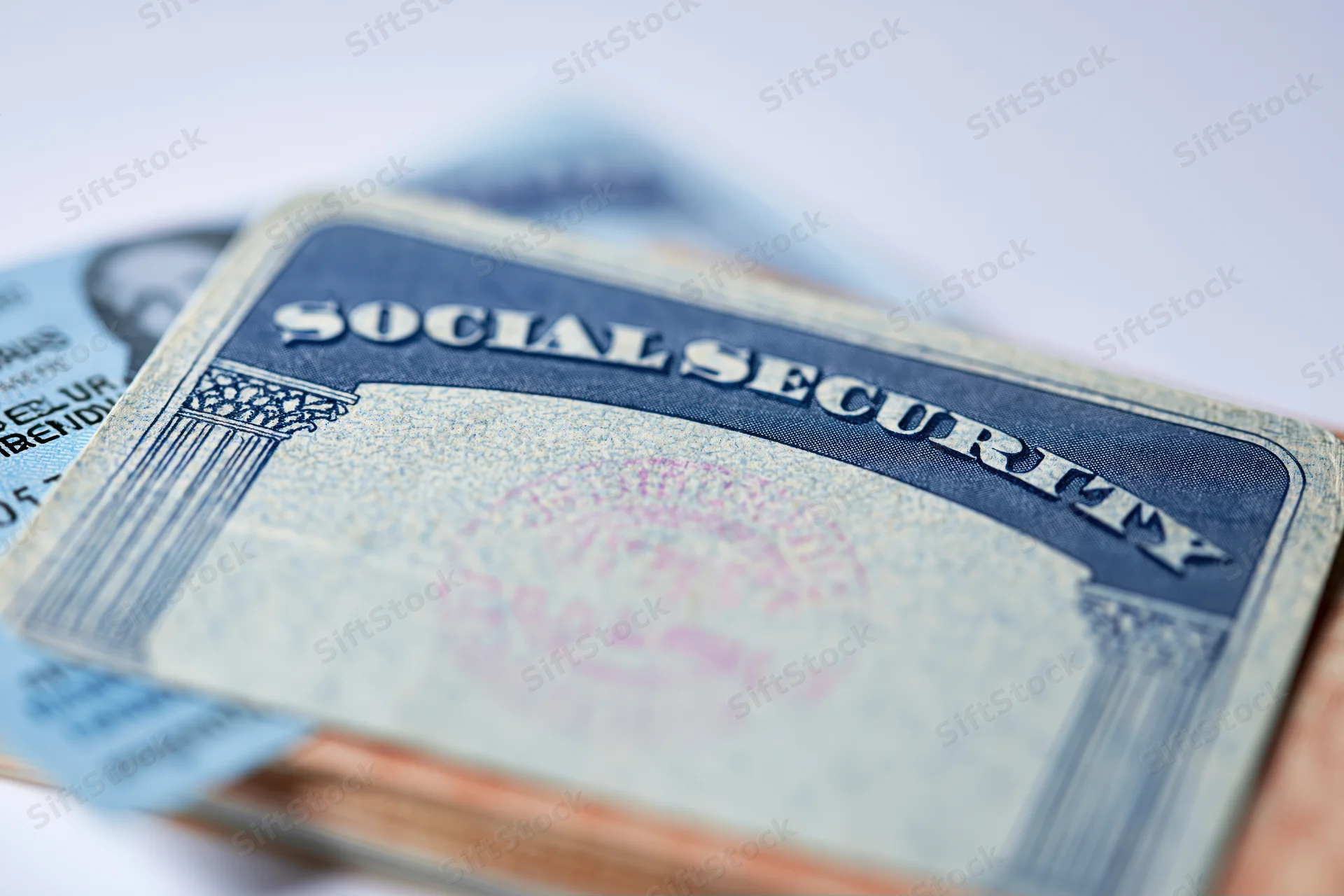 Social security card resting on blurred document with text visible, close-up view on white background