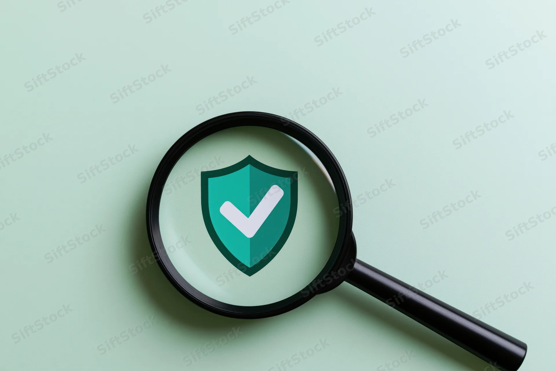 Black magnifying glass over mint-green surface showing shield with checkmark symbol