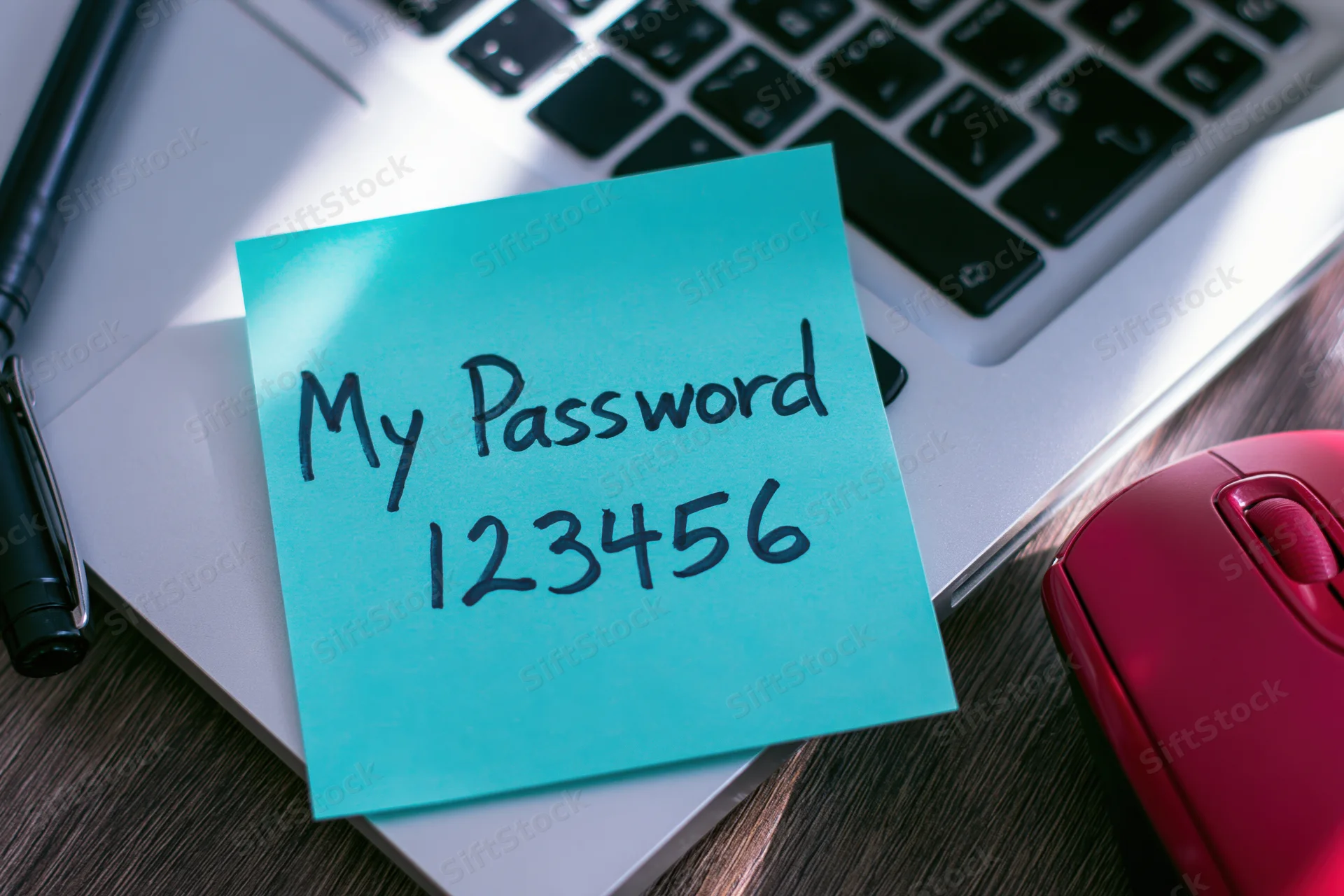 Cyan sticky note with handwritten password 123456 on laptop keyboard near mouse and pen