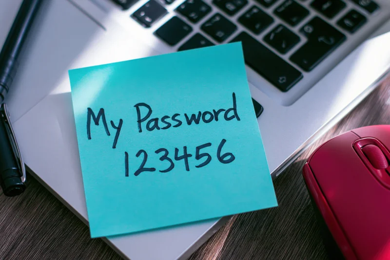 Cyan sticky note with handwritten password 123456 on laptop keyboard near mouse and pen
