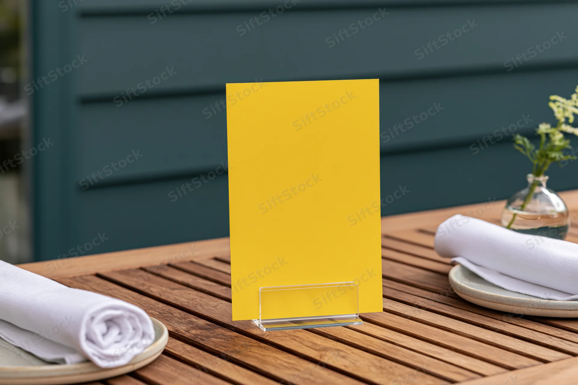 Bright yellow menu card in clear acrylic stand on wooden outdoor dining table with plates and napkins