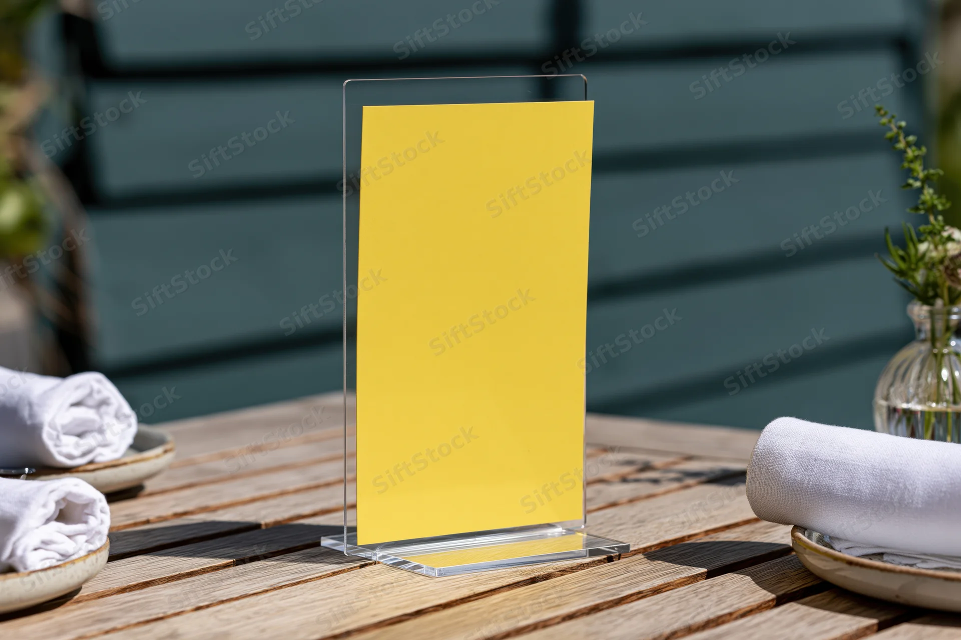 Yellow menu card in clear acrylic stand on wooden outdoor dining table